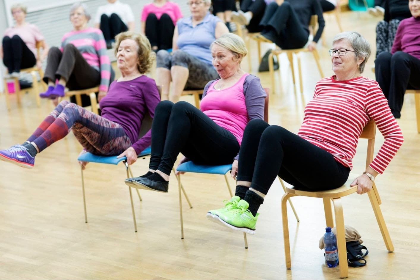 kolme naista istuu tuolilla ja nostaa molempia jalkoja ylös