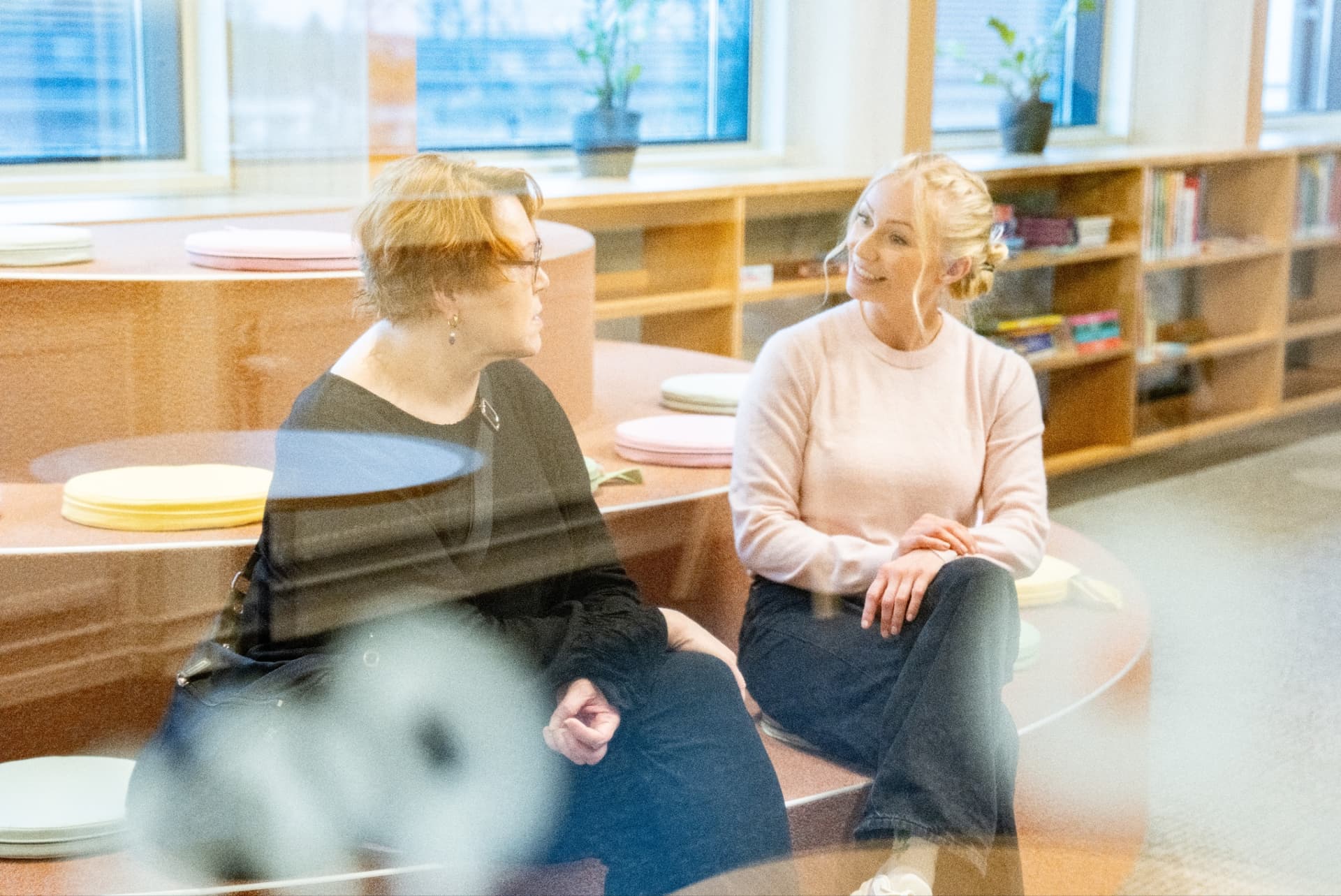 Kaksi aikuista keskustelee kirjastossa leikkiportailla