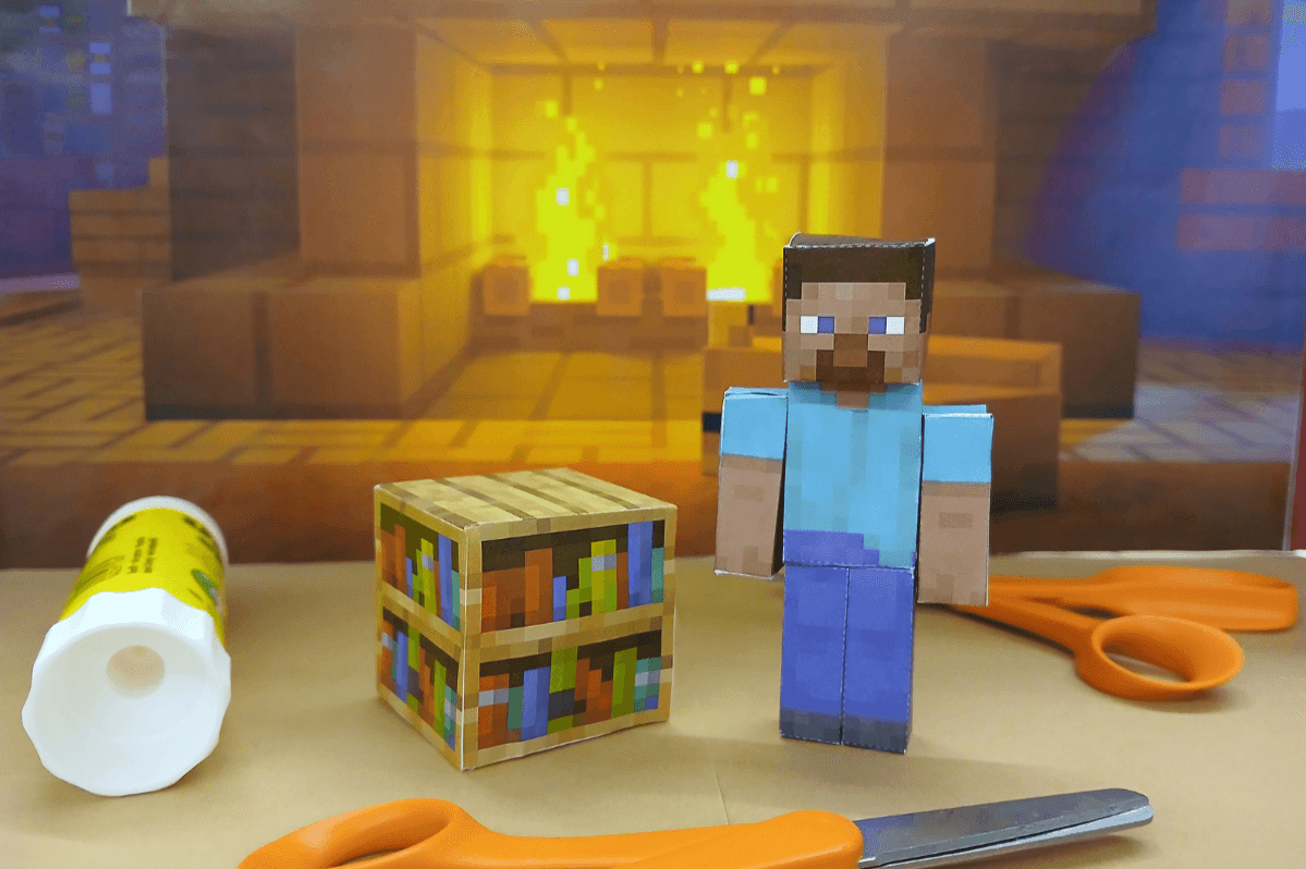 Pöydällä on paperista tehty Minecraft-hahmo, liimapuikko ja sakset