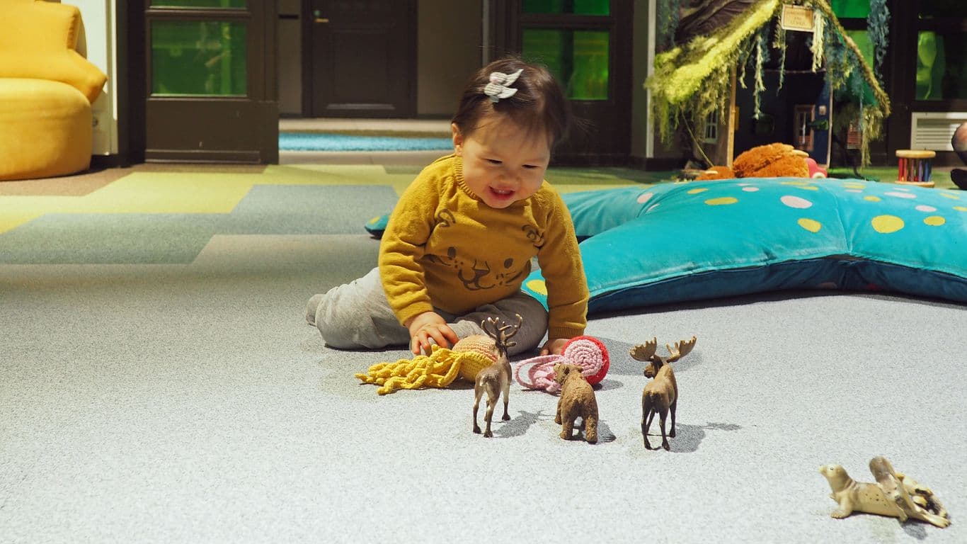 The toddler sits on the floor, laughing and playing with small crocheted octopuses and plastic animals.